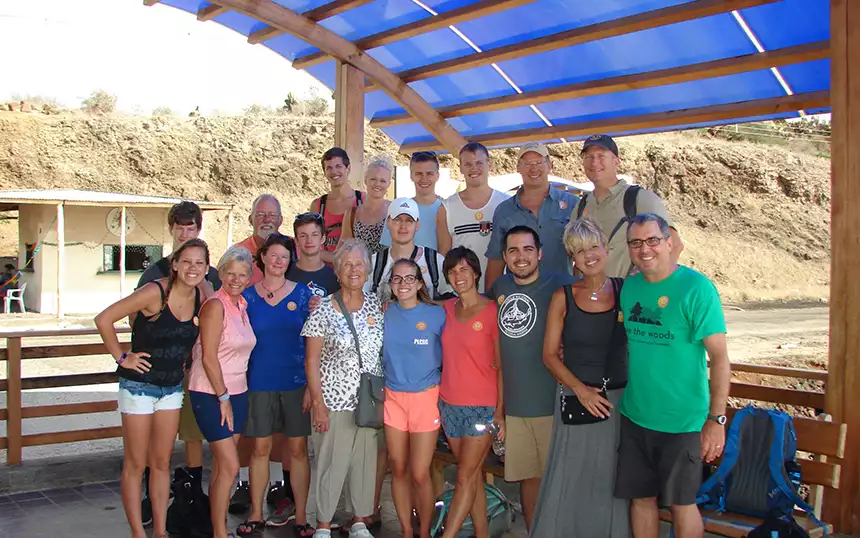 A Galapagos cruise charter group of family members poses on a blue-covered dock with a rocky hillside behind them