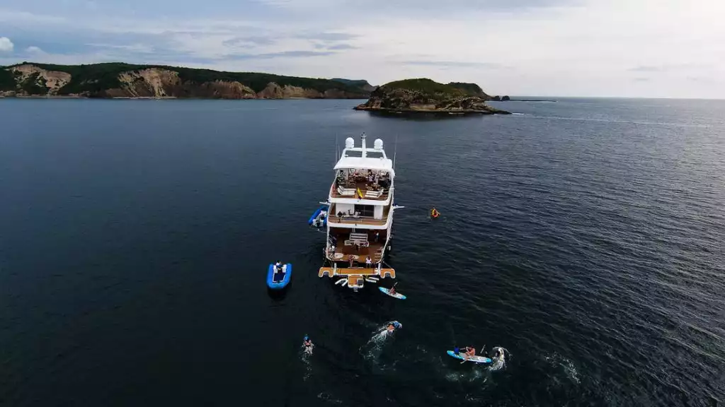 Aerial view of Kontiki Wayra yacht at a swim stop in Costa Rica with empty blue tender & guests on paddleboards & swimming.