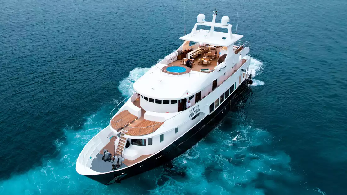 Aerial view of Kontiki Wayra yacht with dark blue hull, 3 white upper decks, teak decking & large Sundeck Jacuzzi.