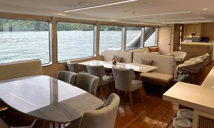 Indoor dining area with marble tables and grey chairs aboard small cruise ship with large windows to watch the water 