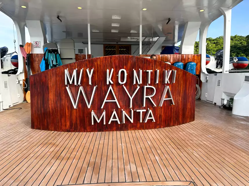 A wooden sign that says M/Y kontiki wayra manta on the back of a small cruise ship with activity gear around ready for guests to swim and kayak 