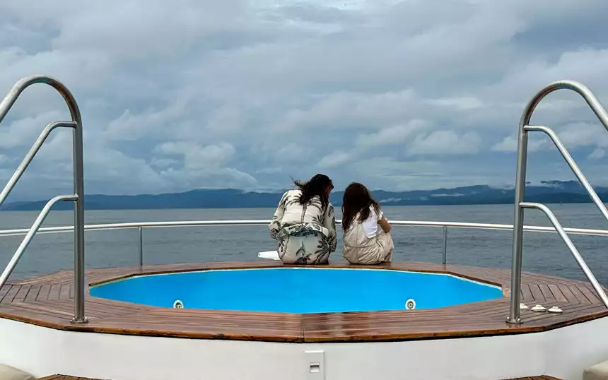 Mother and daughter sit on the end of a small cruise ship hot tub looking out at the stormy clouds 