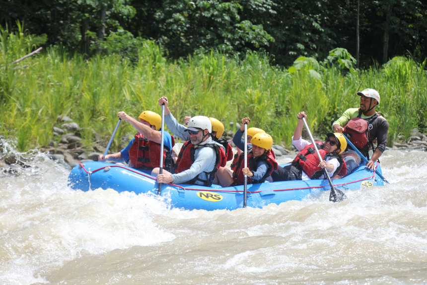 Adventurist kayaking through strong waters in a blue raft with red life jackets and yellow helmets as they paddle