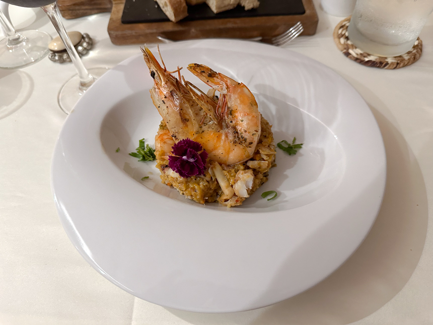 Shrimp and rice beautifully plated on a white plate with a purple flower on a white table