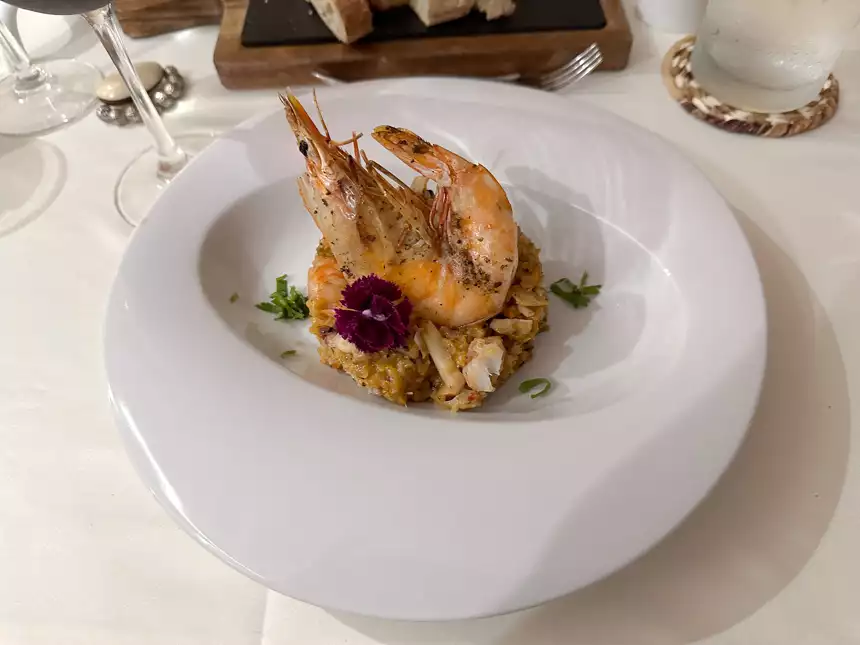 Shrimp and rice beautifully plated on a white plate with a purple flower on a white table