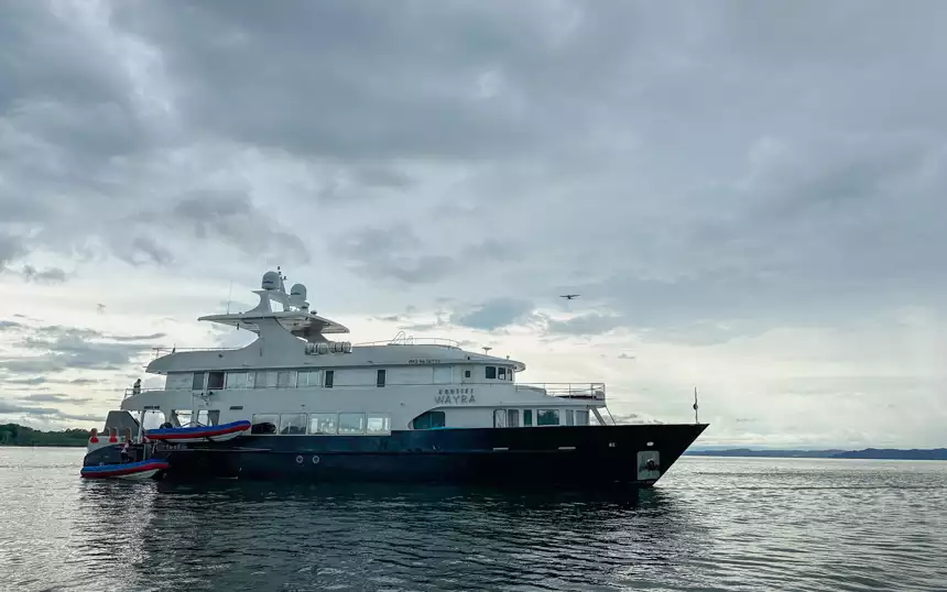 blue and white Small cruise ship on a stormy day with grey skys with two skiffs on the side and a plane flying right over