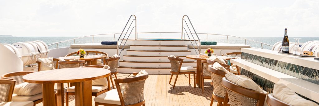 Sundeck aboard small cruise ship with luxury seating and a bar ready for guests to use with starirs leading to a hot tub on the bow