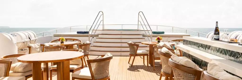 Sundeck aboard small cruise ship with luxury seating and a bar ready for guests to use with  starirs leading to a hot tub on the bow 