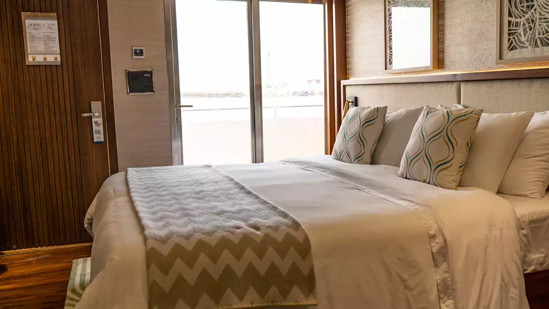 Veranda Stateroom with king bed in white sheets & beige throw blanket with floor-to-ceiling window & nature-inspired decor.