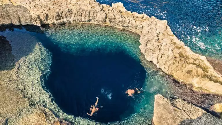 Aerial view of 2 Malta cruise guests swimming in a dark blue caldera beside open ocean during the La Dolce Vita cruise.