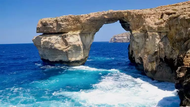 Sea cliffs formed into an arch on the coast of the med with bright blue waters