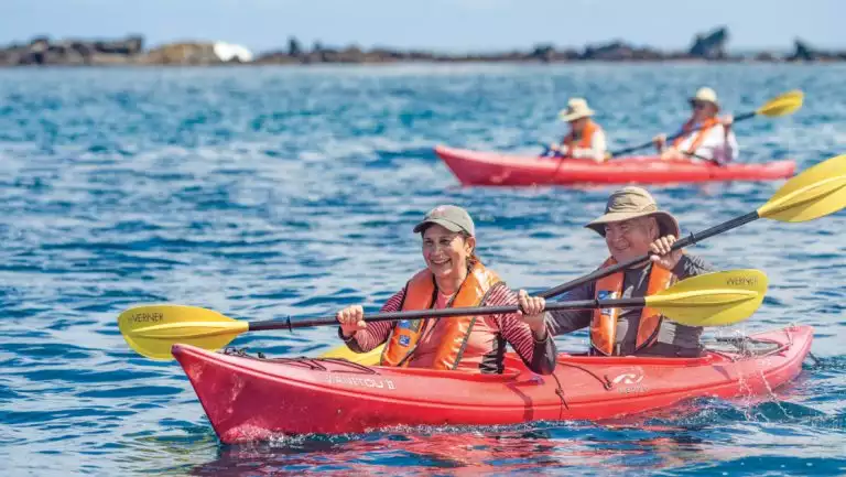 Guests on a Nat Geo Galapagos by Catamaran cruise explore the Buccaneer Cove in tandem red kayaks at Santiago Island.