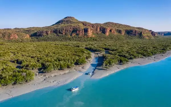Two small Australia cruise ships seen from above sailing into the Hunter River in the remote Kimberley with green trees and blue water