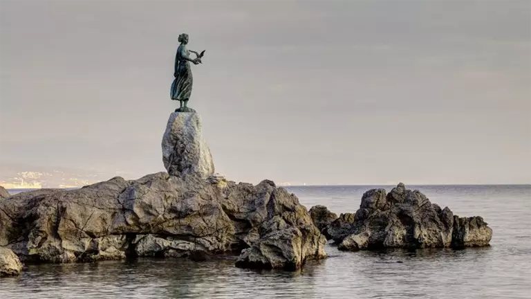 Statue looking out into the water on rocks on a calm grey day