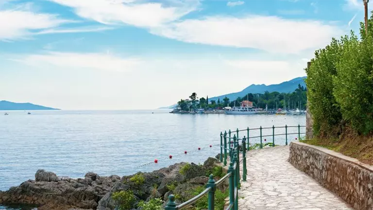 A paved walkway around a beautiful lake on a still day surrounded by green trees and rolling hills.