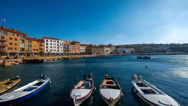 day boats lined up in a Croatian harbor with colorful buildings surrounding calm waters in the bay on a sunny day