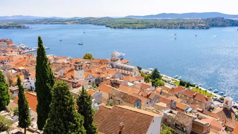 ariel view of sibenik croatia with tan building's and red roofs overlooking the beautiful waterway with boat cruising about