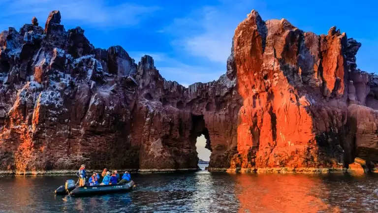 Black Zodiac boat with Baja California Discovery cruise guests drifts beside eroded white & white canyon walls at sunset.