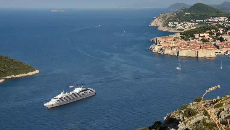 Aerial view of small gray expedition ship cruising into port at Dubrovnik, Croatia with its terra-cotta-roofed buildings.