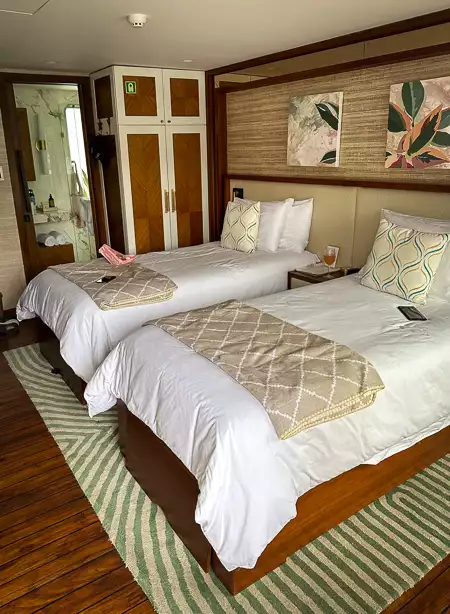 Inside of cabin aboard small cruise ship with 2 double beds with white sheets and wooden accents around the room