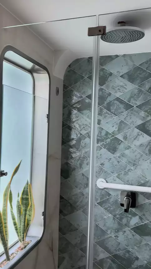 bathroom shower with rain showerhead and stone tile with a large window to look out and plants for nice vibes