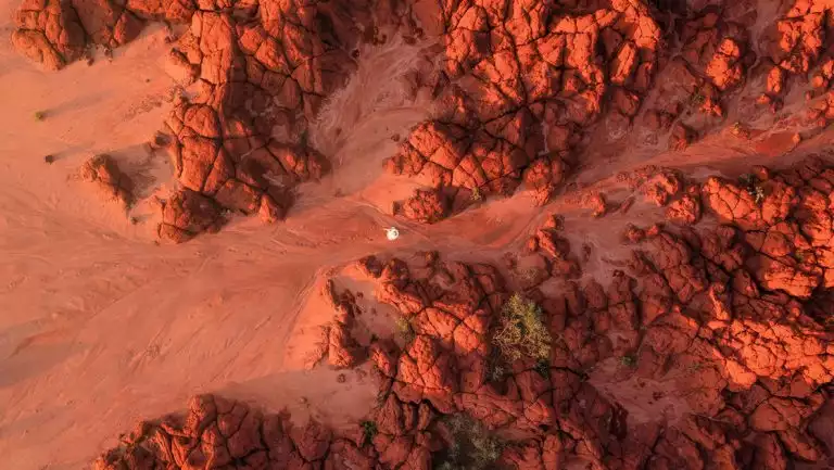 Aerial view of PASPALEY PEARL Pealing Coast cruise guest walking red-sand beach among chunky red rocks in Australia's Kimberley.