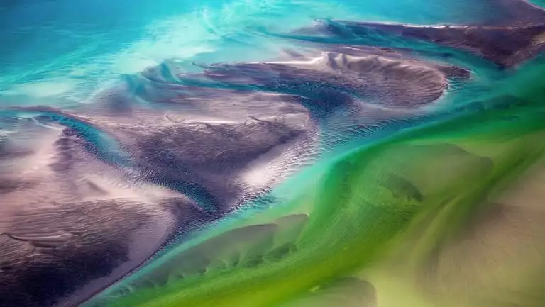 Aerial view of the Kimberley region of northern Australia with tides creating melting colors of green, teal & purple.