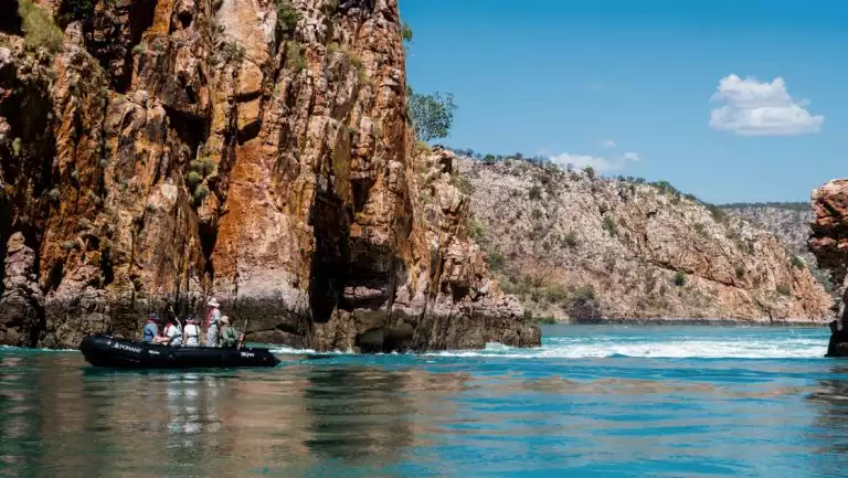 Black Zodiac boat with PASPALEY PEARL Rowley Shoals & Kimberley Cruise guests motors between chunky rock cliffs in Australia.