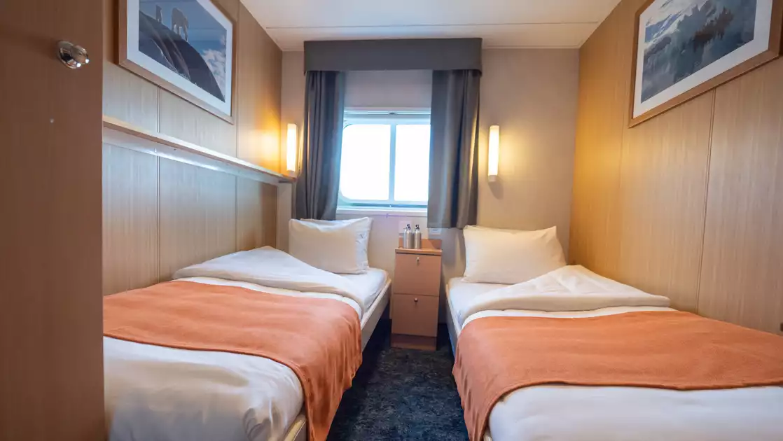 2 twin beds in white & salmon-colored linens by window & wood bedside table in Twin Cabin aboard Quest Arctic expedition ship.