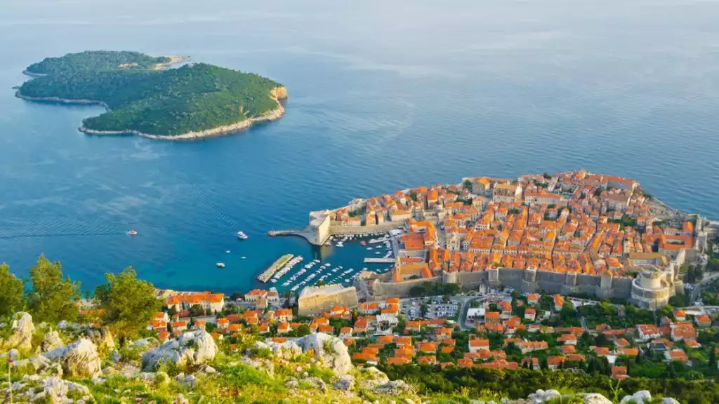 Ariel view of coastal Mediterranean town with red roofs and a small isalnd near by