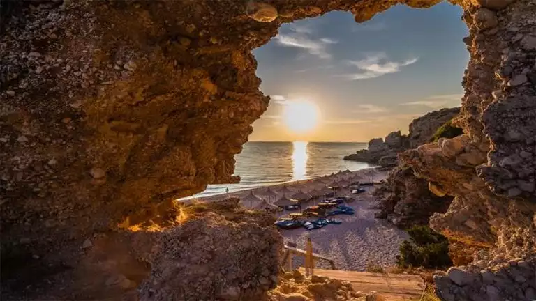 Sunset view through rocks that create an opening looking onto a beach with a sunset over the ocean