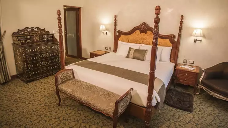 Doubled bedroom with white bed sheets and a traditional classic look with a bench at the end of the bed at Aranwa Cusco boutique