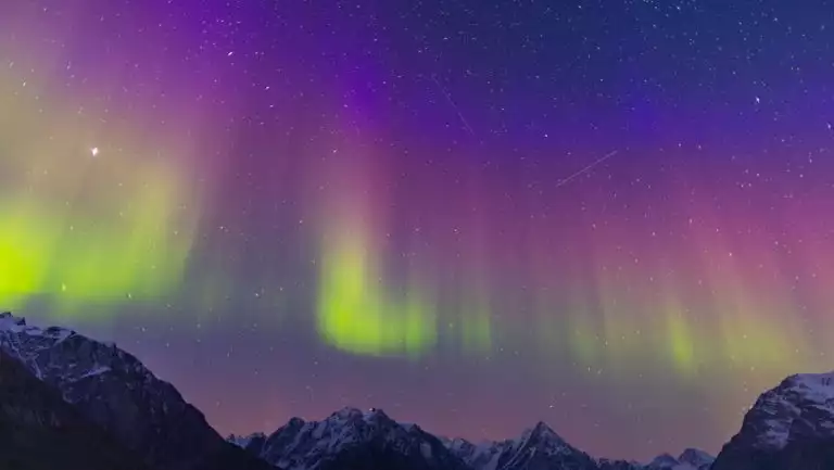 Northern Lights in green, pink & purple shine above jagged peaks during the Arctic Golden Autumn expedition cruise.