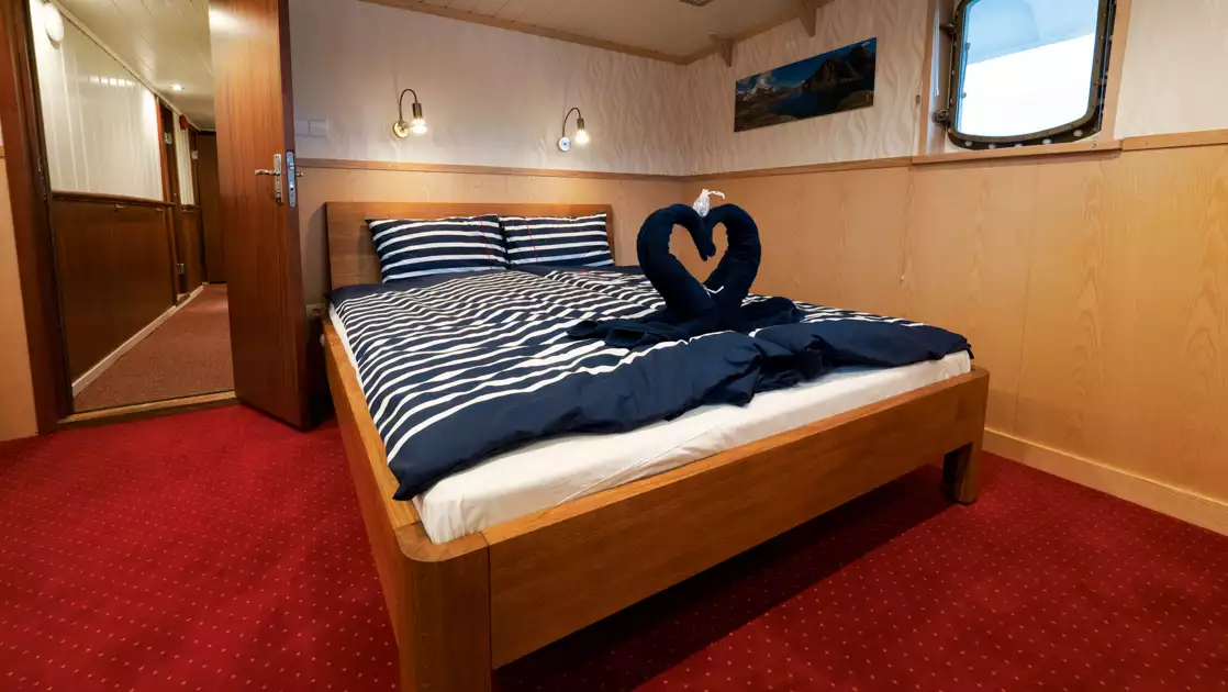 Double Cabin Superior on MS Sjoveien with double bed in nautical colors atop red carpet & under reading lights & view window.