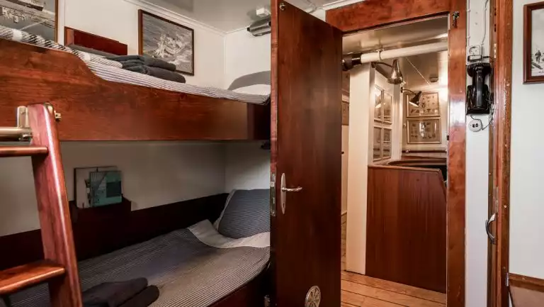 Cabin 25 on MS Stockholm ship with wood bunk beds in nautical bedding, framed photos, white walls, wood trim & door to lounge.