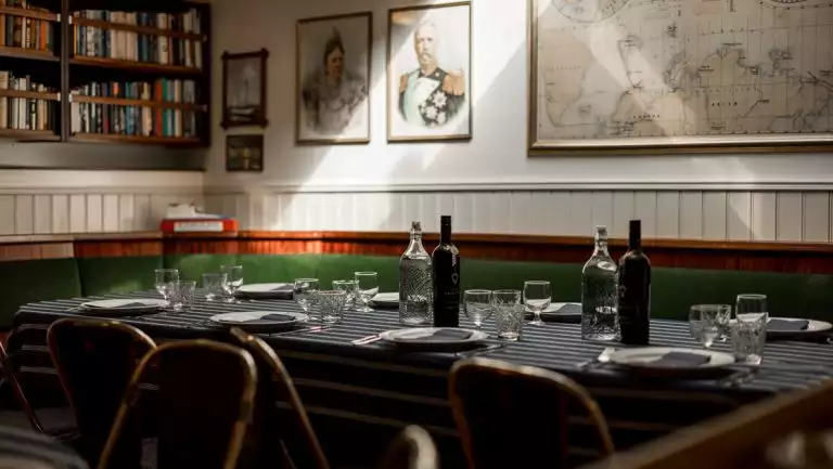 Nautical themed dining room on MS Stockholm with blue tablecloths, white bead board, green bench seat & books, set for a meal.