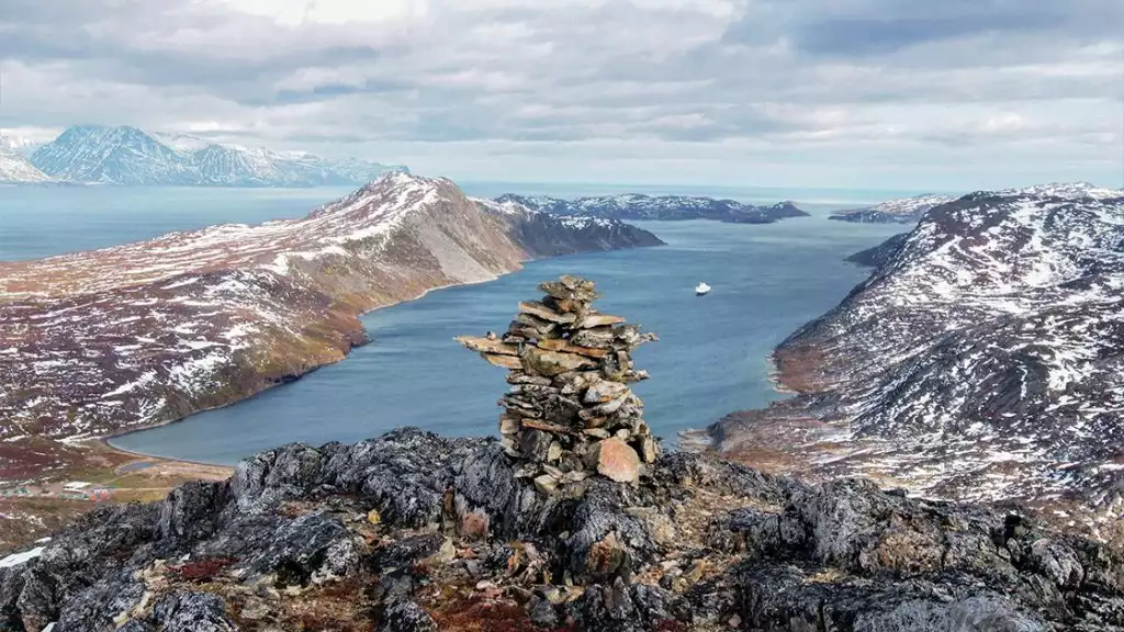 Stacked rocks on the top of am overlook looking down into the bay of water with a small ship off in the distance