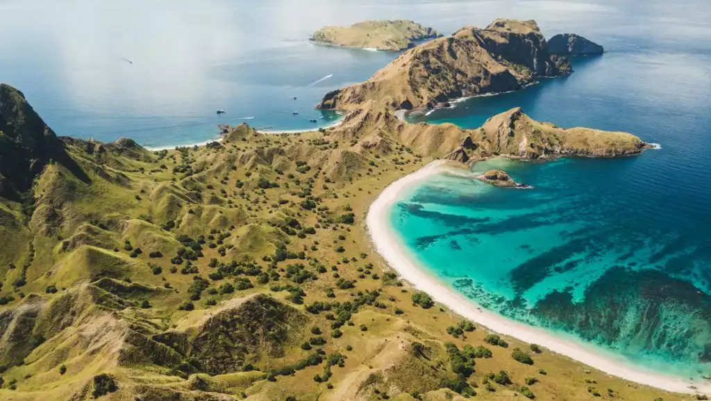 Aerial panoramic view of Padar island in Komodo National Park, Indonesia, with green hills, white-sand beach & tropical sea.