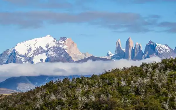 showcasing the patagonia climate on a sunny day with large jagged mountains jutting out of the fog with blue sunny sky above