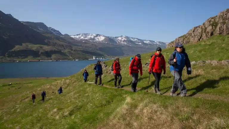 Small group of Scotland, Faroes & Iceland travelers in red & blue jackets walks up a singletrack trail on a grassy hillside.