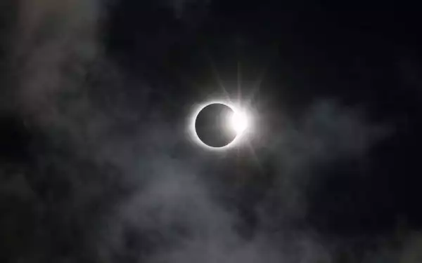 Black night sky with some clouds and sun nearly eclipsed by the full moon.