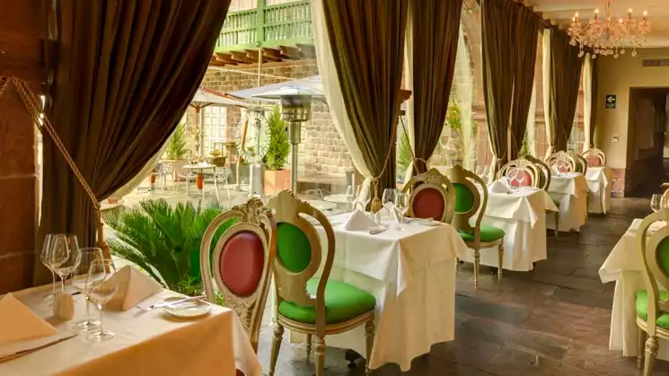 Luxrious dining at the Aranwa Cusco boutique hotel with dark drapes white linnen tables with red and green unique chairs