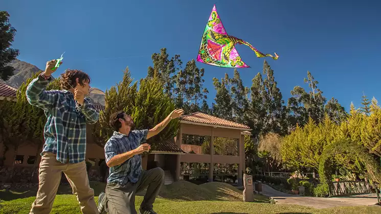 Father and son fly a pink and green kite in front of the Aranwa Sacred Valley Hotel surrounded by green trees