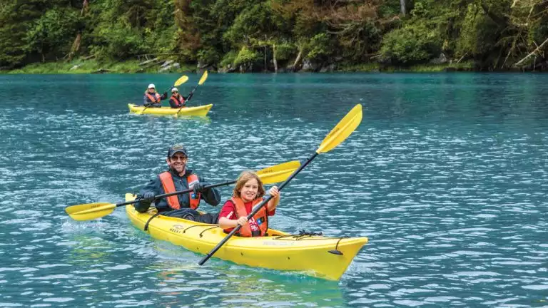 A family of four explores in yellow kayaks and red life vests in Alaska, USA