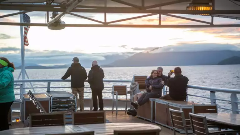 Group of travelers gather at the back of the boat to enjoy the sunset off the top deck and snap some pictures