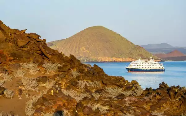 National Geographic Endeavour II Galapagos cruise ship seen at anchor near Bartolome island amid red and tan rocky hillside