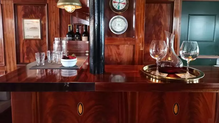 Tray with 2 wine glasses & decanter sits atop mahogany wood bar with inlaid gold details on MS Balto Arctic yacht.