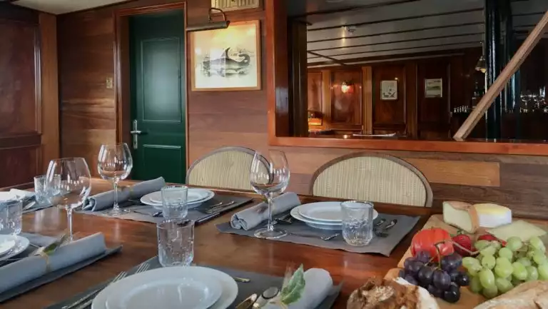 Dining area of MS Balto with place settings of glasses, dishes, napkins & charcuterie board surrounded by wood decor.