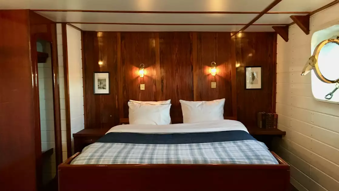 Double cabin on MS Balto with fixed double bed, wood & white walls, reading lamps & porthole.