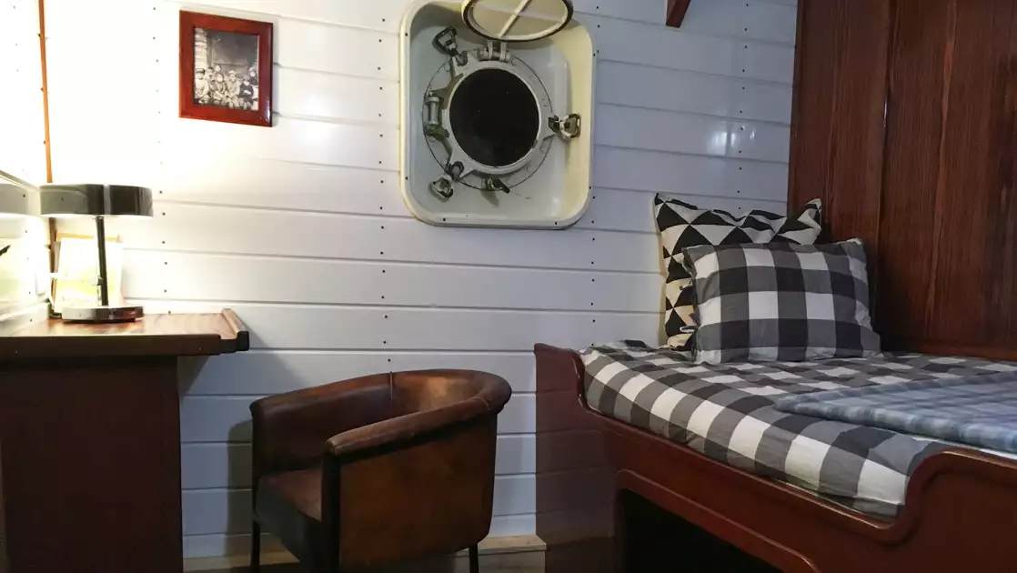 Single cabin on MS Balto with fixed twin bed, white & wood walls, portholes, small wooden desk & leather chair.